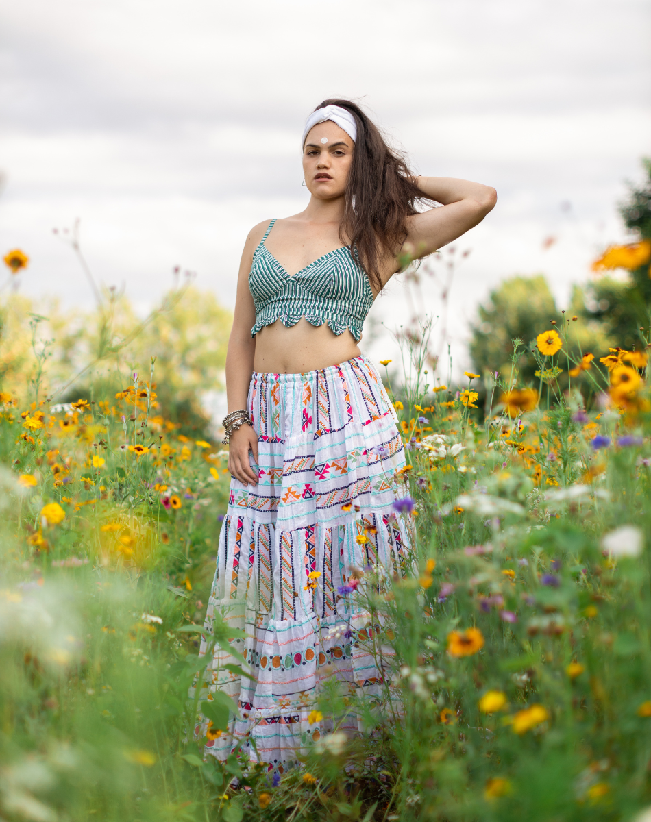 Woman in a green sustainable top and patterned skirt standing in a field of wildflowers promotion sustainable fashion.